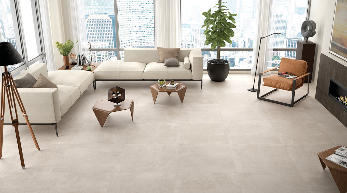 KTL Claire Arena 100x100 cm en salón con sofás, chimenea y ventanal, suelo porcelánico efecto cemento